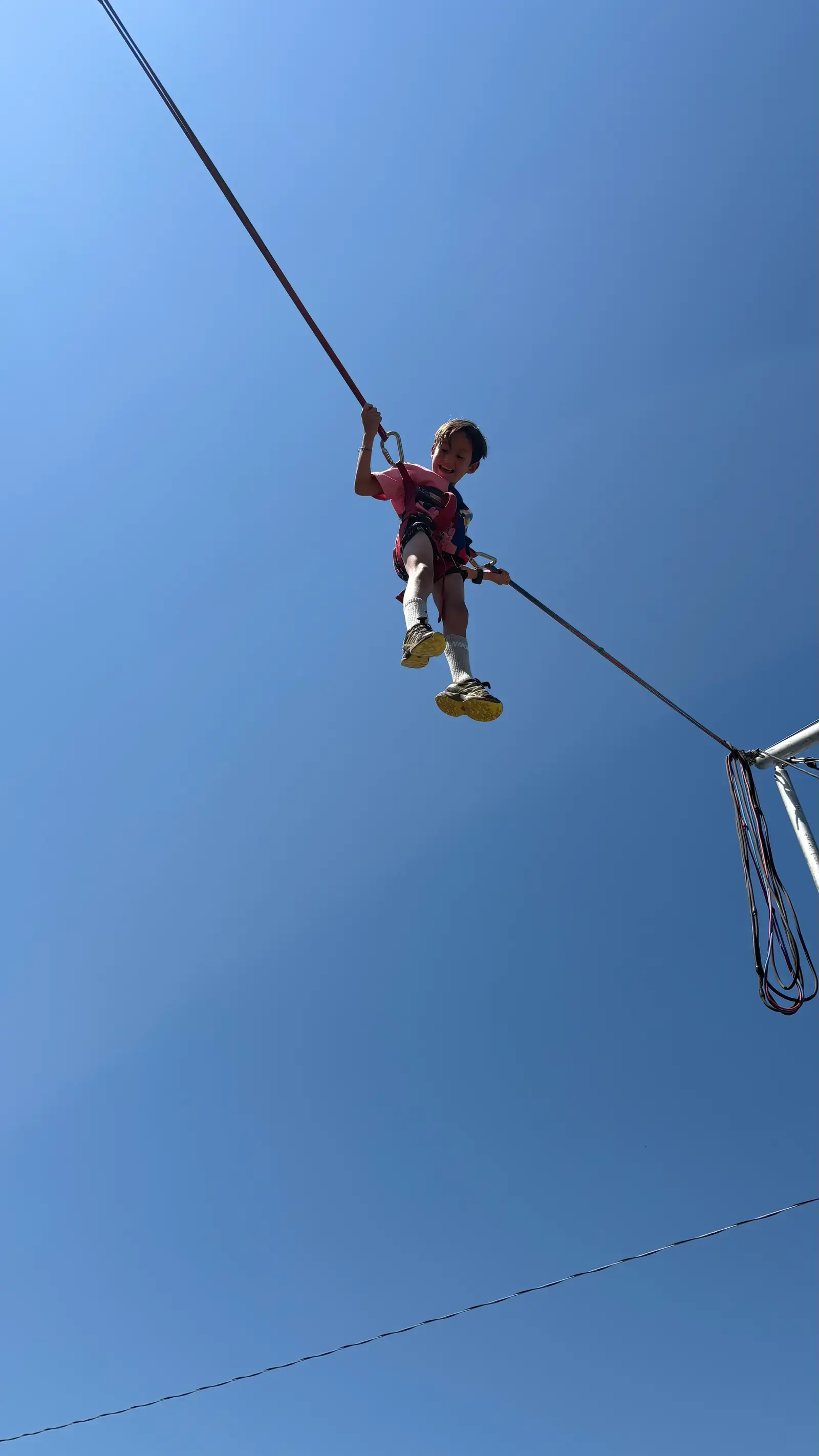Camper mid-air on the on-site bungee trampoline against a blue sky
