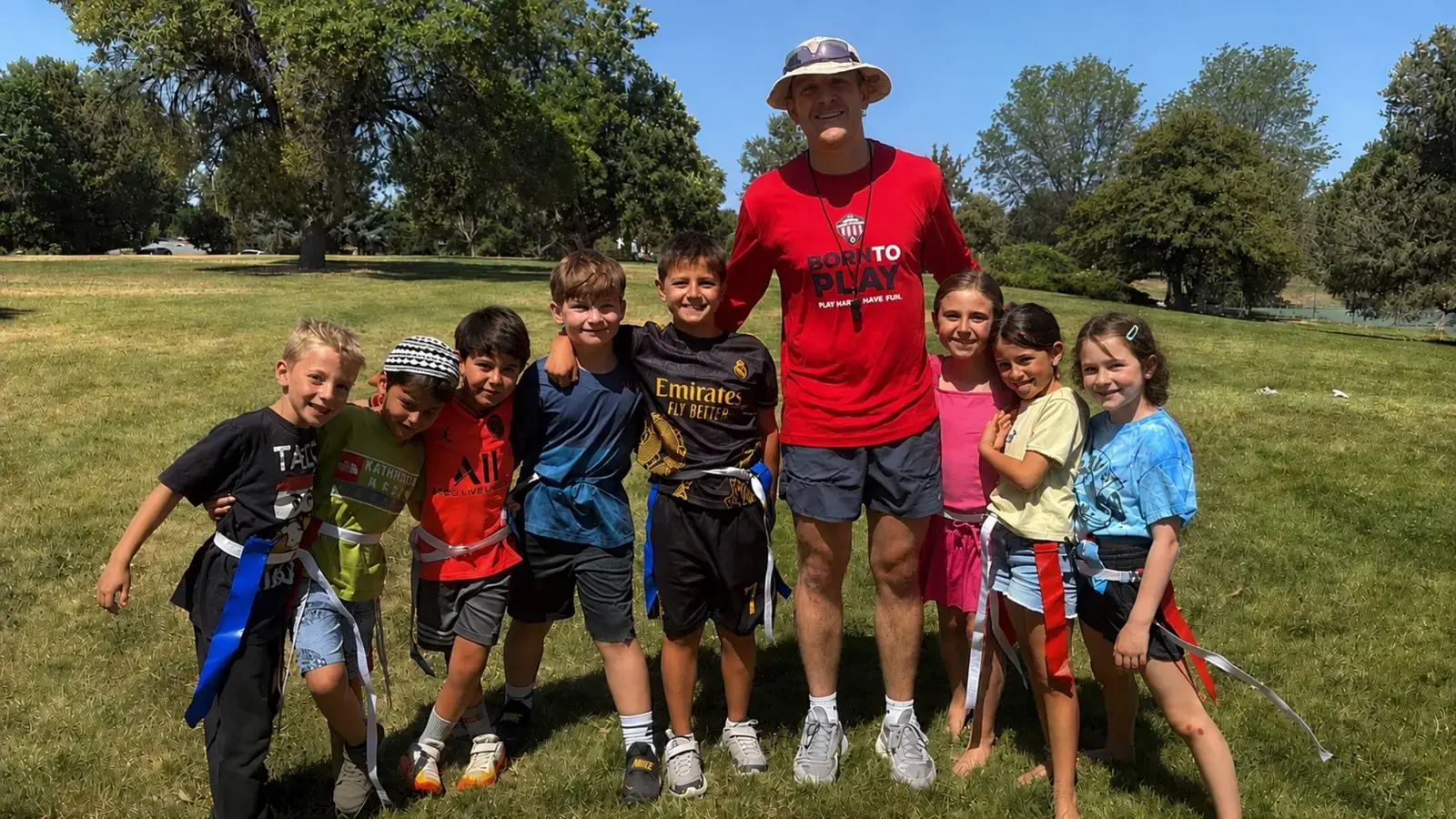 A sports coach with a group of campers wearing flag-football belts on the field