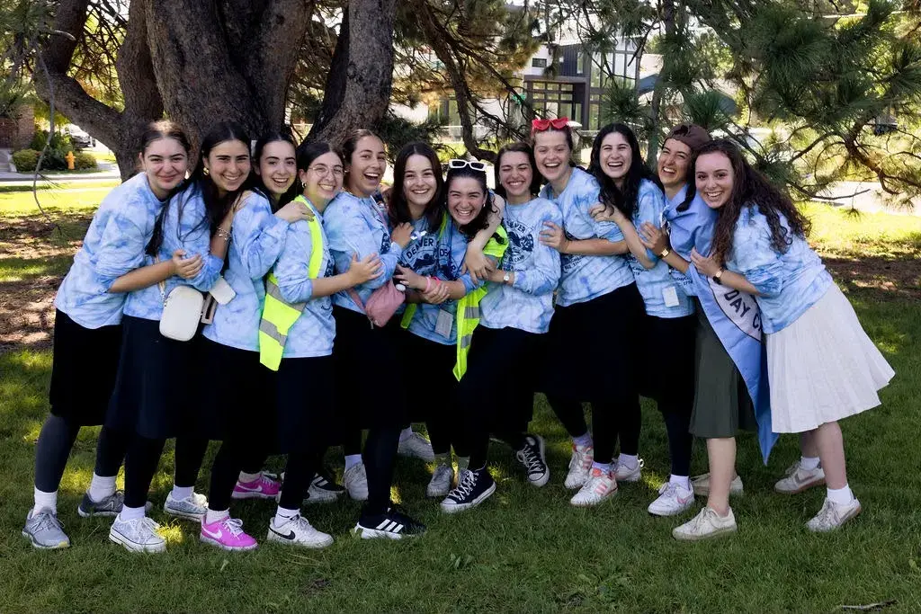 Denver Jewish Day Camp counselors in tie-dye camp shirts, arms around each other and laughing together under a tree
