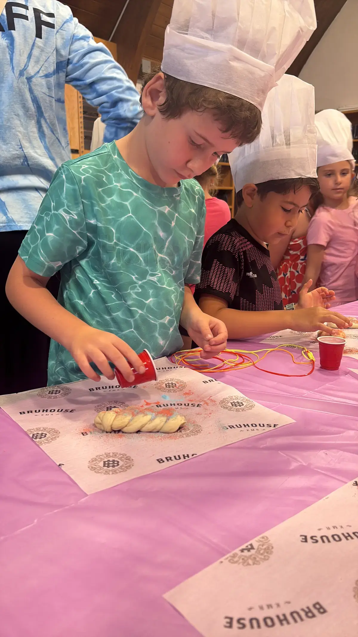 Small hands shaping challah dough at the baking table