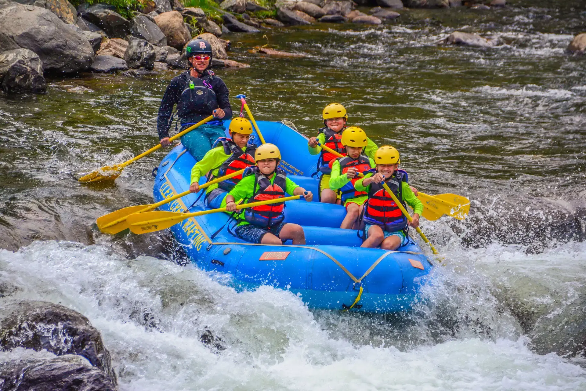 Campers in helmets and life jackets paddling a raft through whitewater rapids on a Denver Jewish Day Camp trip