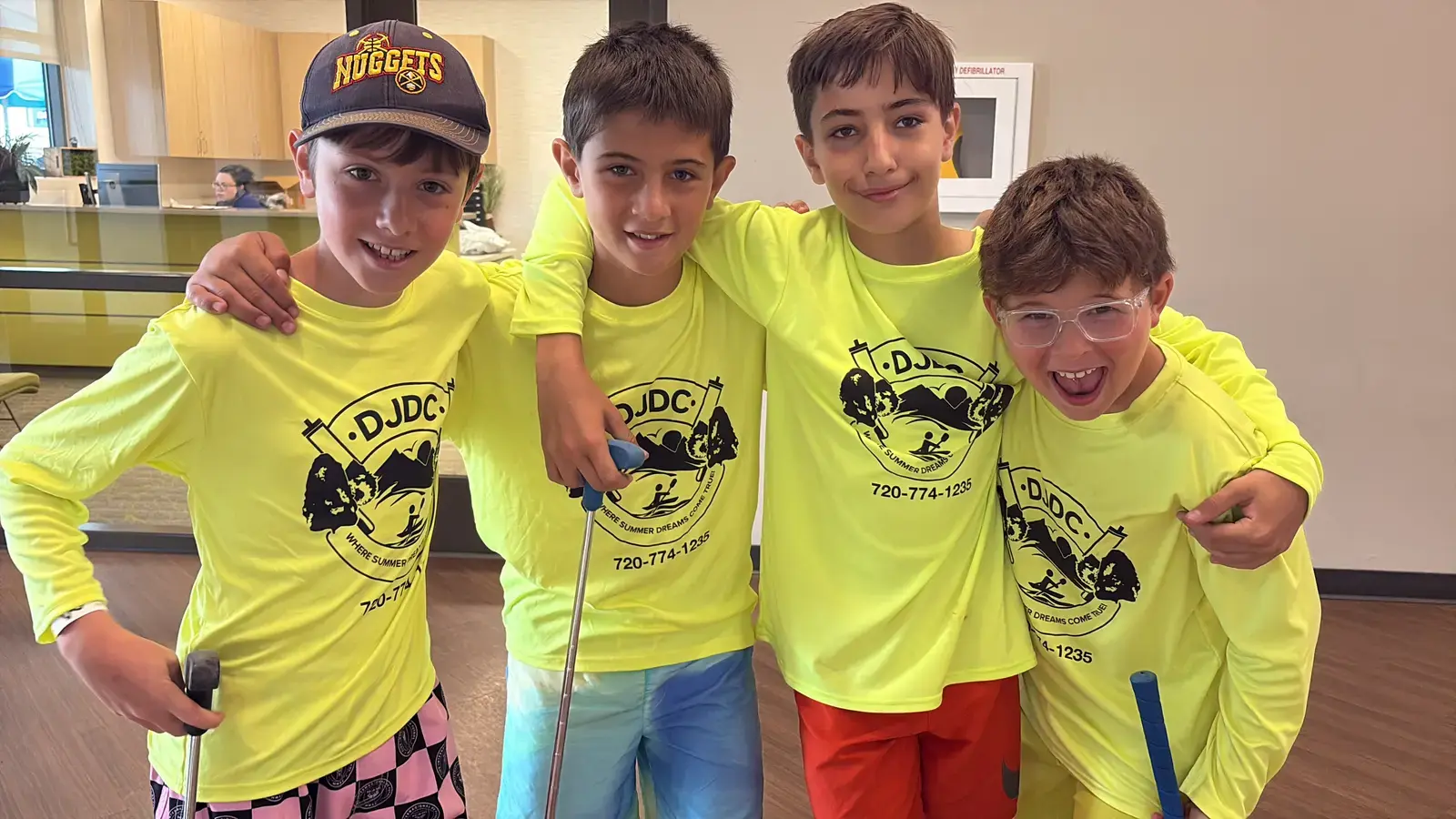 Four senior campers in neon DJDC shirts with golf clubs, arms around each other