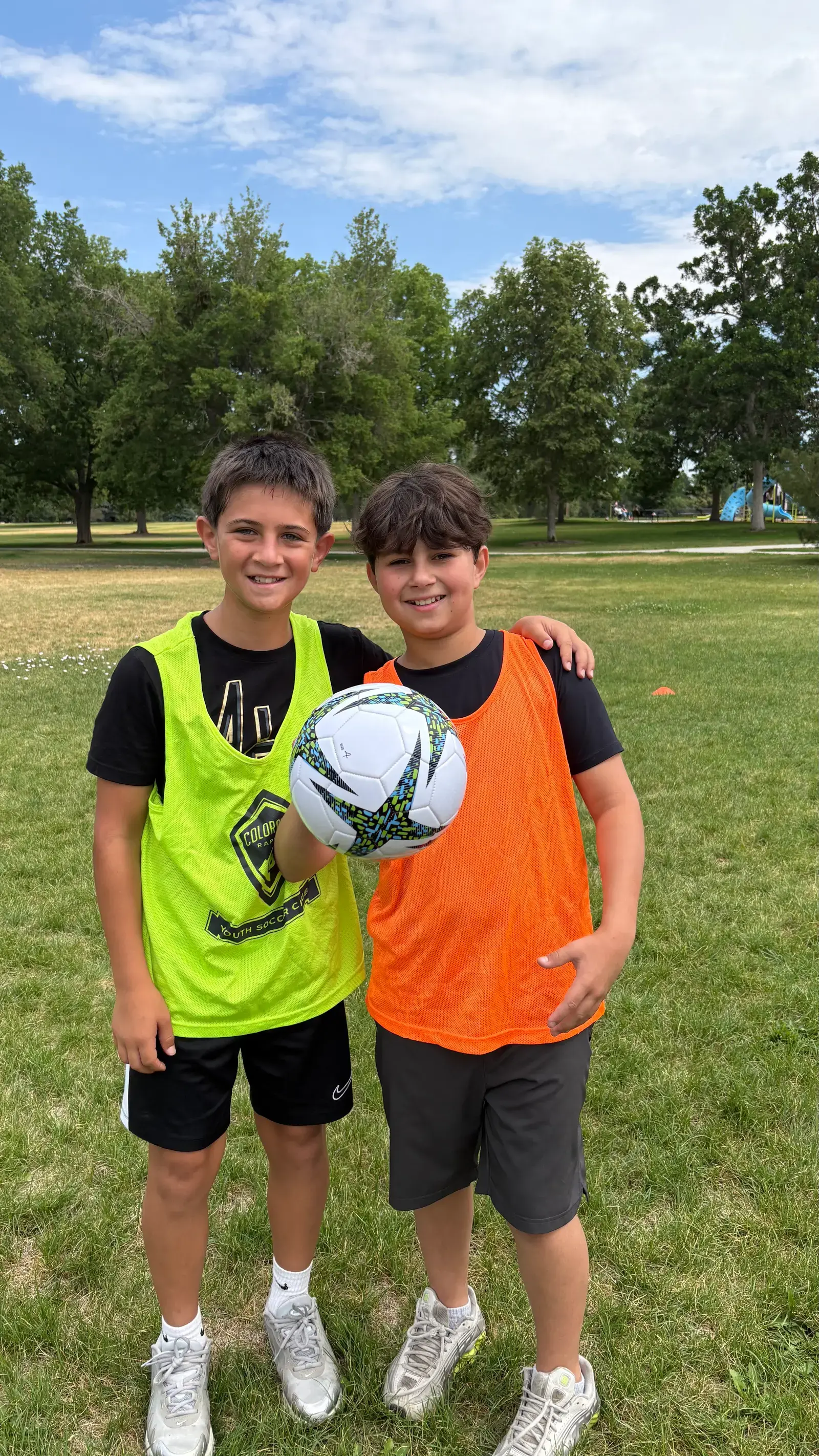 Two campers in green and orange pinnies holding a soccer ball on the camp field