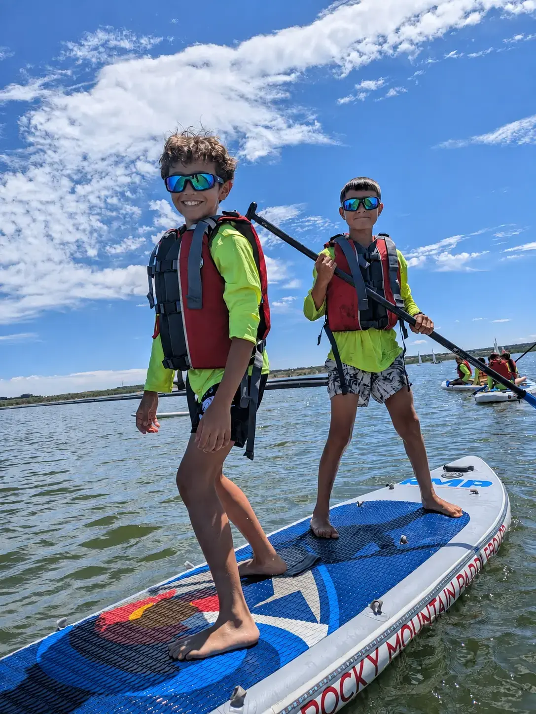 Two campers paddleboarding on the reservoir in life jackets